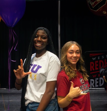 Camryn and Emma throwing up their perspective college hand gestures at Signing Day.